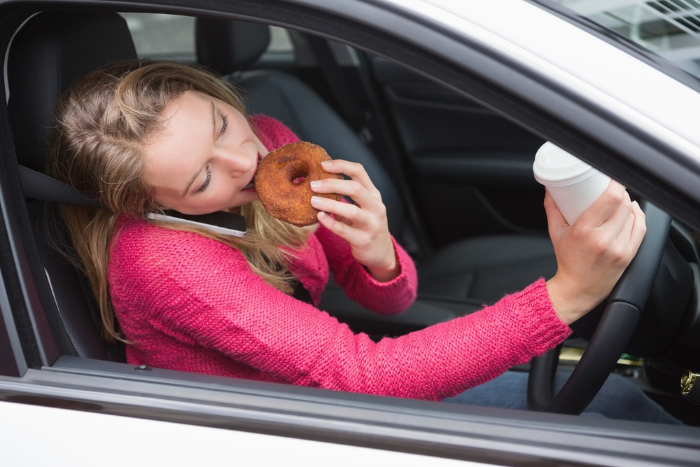 Young woman having coffee and doughnut in her car